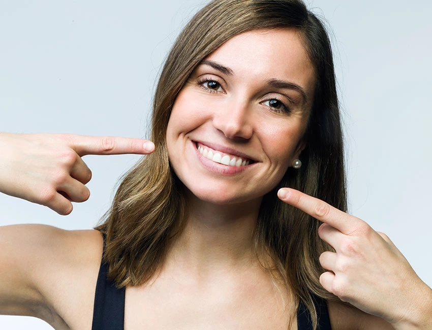 Patient pointing to her smile after teeth whitening