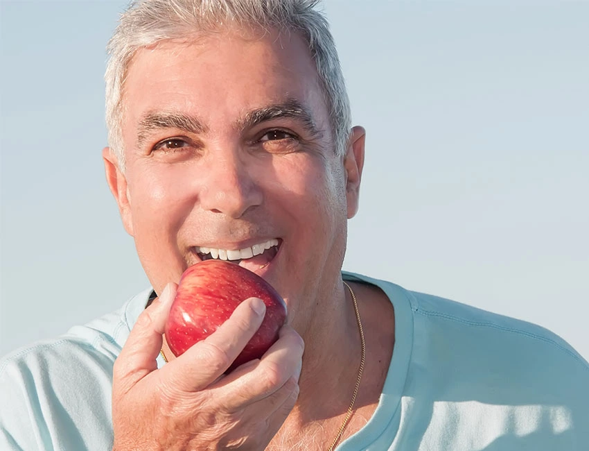 Happy patient biting an apple after couple months getting dental implants in Agoura Hills, CA